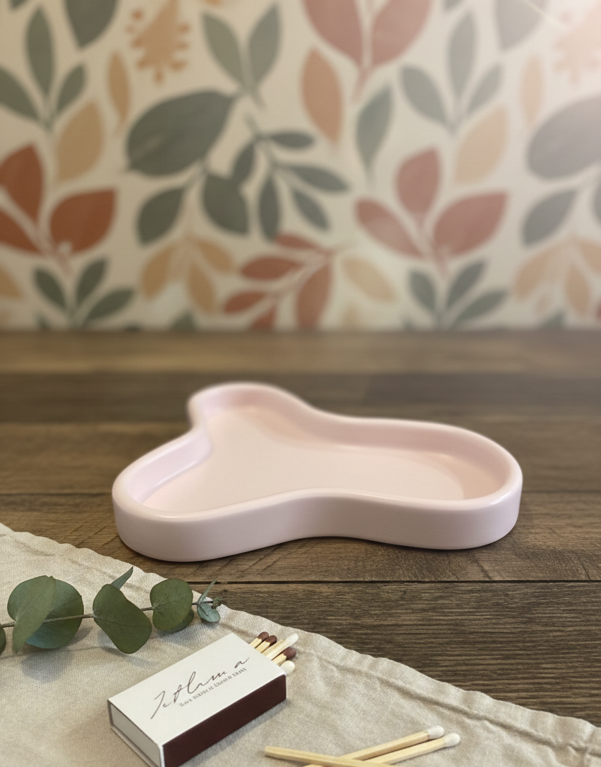 Pink ceramic dish on a wooden surface with matches and greenery, against a patterned wall.
