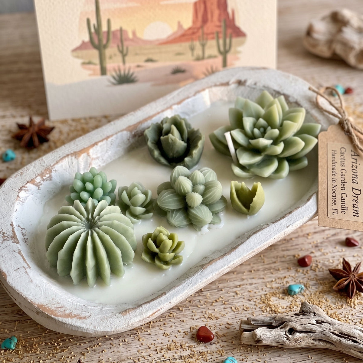A styled product shot of a white ceramic dish holding several green succulent-shaped items, with a desert landscape print card and a paper tag reading 'Diffused Dream' in the background on a rustic wooden surface.