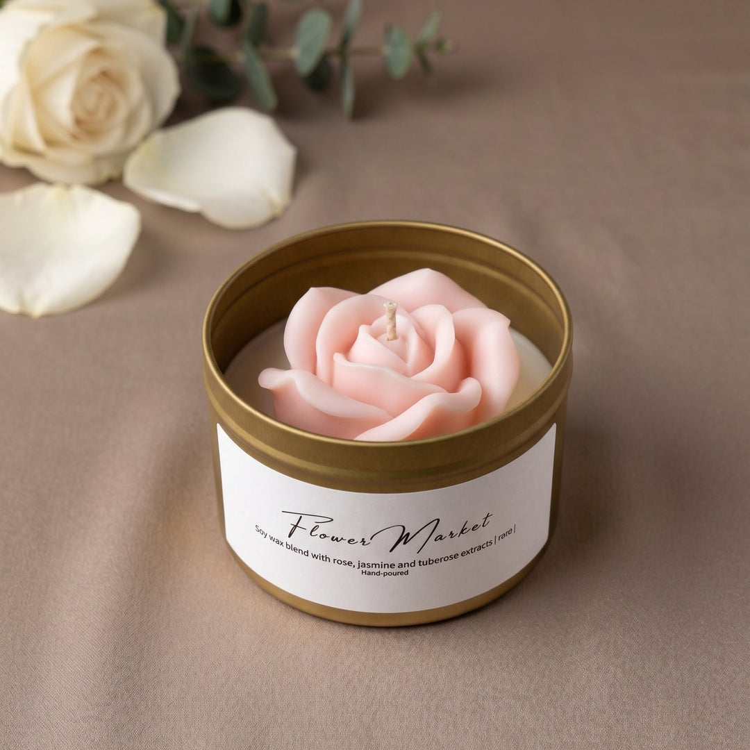 A pink rose-shaped candle in a gold metal tin with a white label reading &