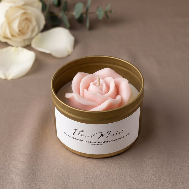 A pink rose-shaped candle in a gold metal tin with a white label reading &