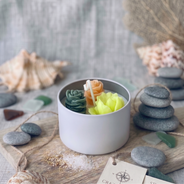 Candle with succulent-like wax in a white container on a textured surface with seashells and stones.