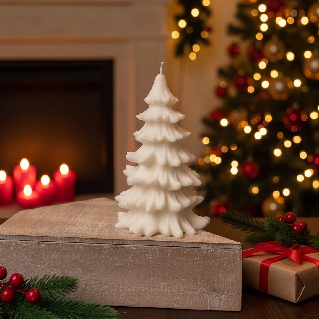 A white Christmas tree-shaped candle displayed on a rustic wooden box in a cozy holiday setting with a lit fireplace, a decorated Christmas tree, and a wrapped gift in the background.