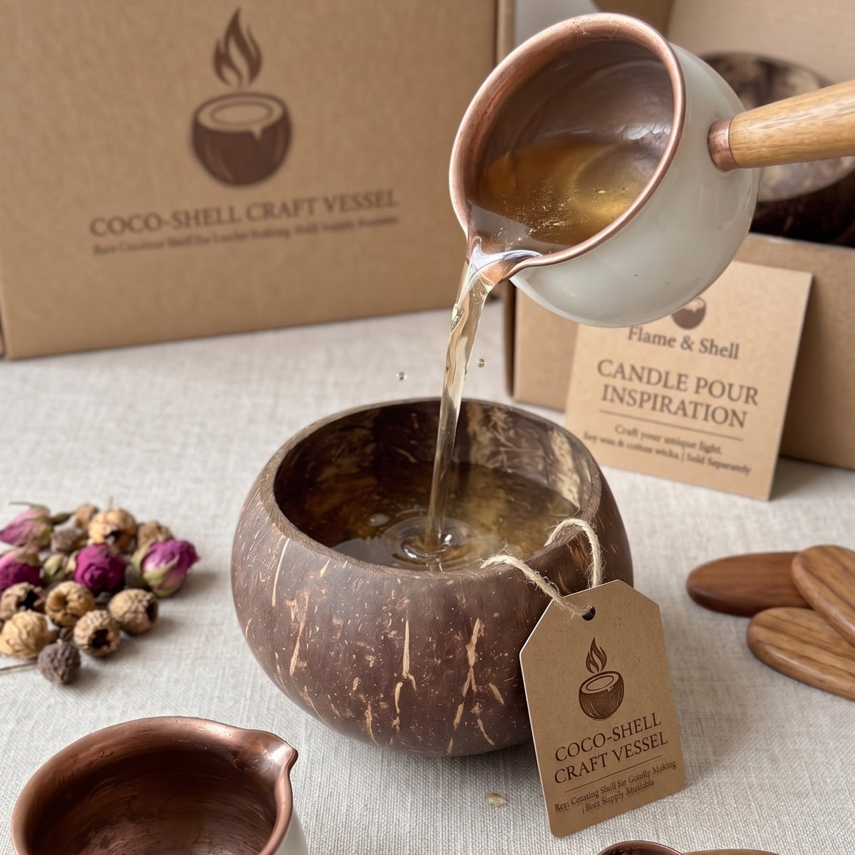 Coco-shell craft vessel set with a coconut bowl, a white ceramic pourer with copper-toned rim, wooden spoon, dried flowers, and branded kraft boxes on a linen surface.