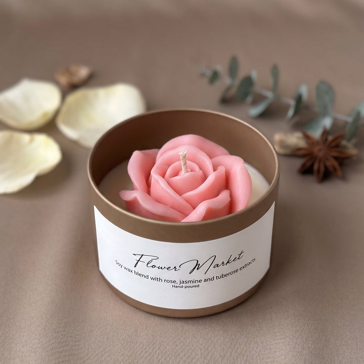 A pink rose-shaped candle in a round brown and white container labeled &