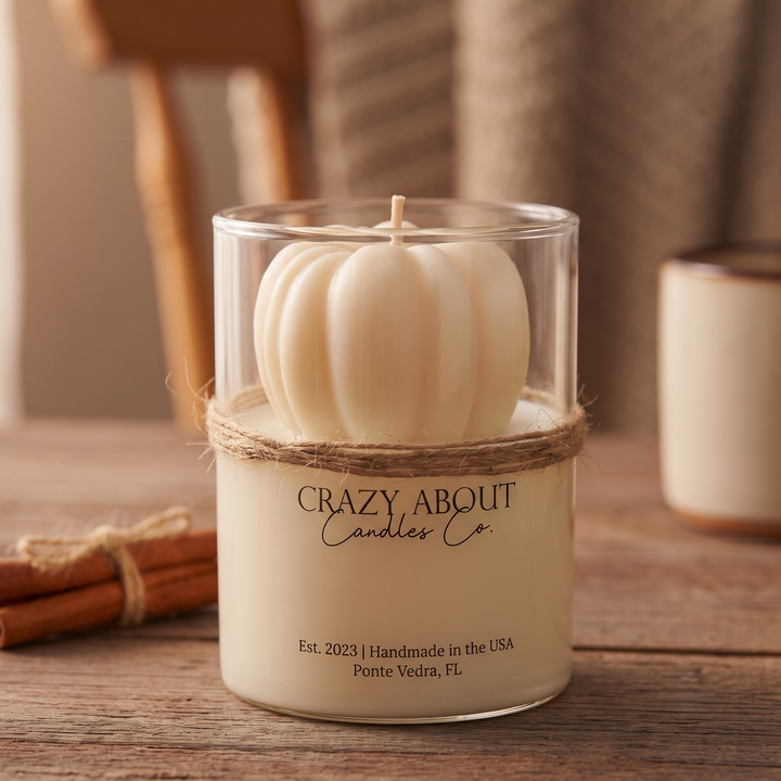 A cream-colored pumpkin-shaped candle in a clear glass jar with a natural twine band, labeled &