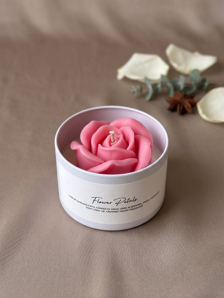 A pink rose-shaped candle in a white cylindrical tin labeled &