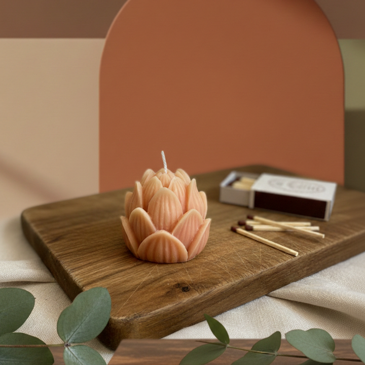 Decorative candle shaped like a flower on a wooden board with matches and green leaves.