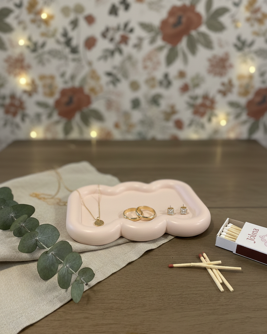 Pink cloud-shaped jewelry tray with earrings on a wooden table with floral wallpaper in the background