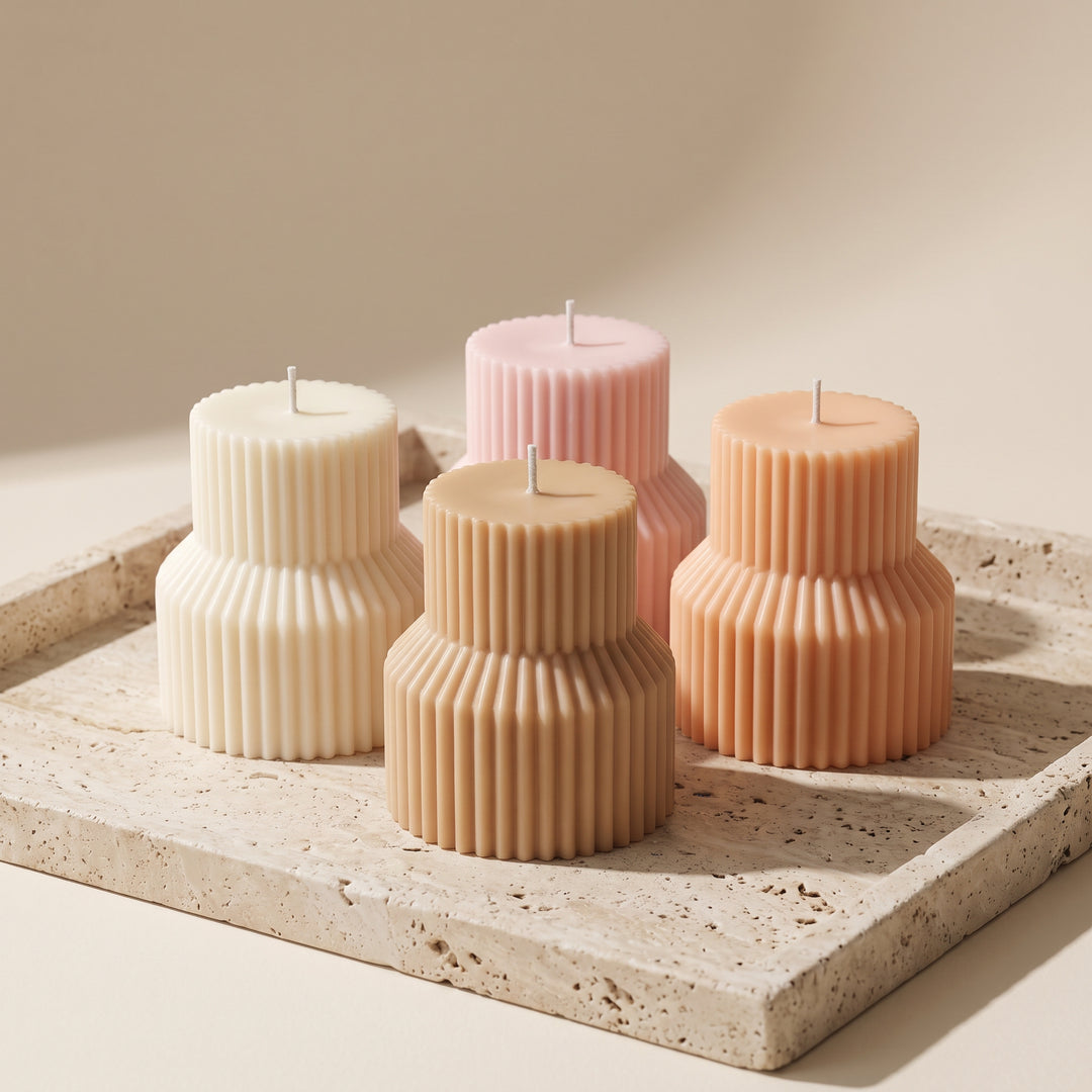 Four ribbed pillar candles in cream, tan, peach, and soft pink, arranged on a light stone tray against a warm beige background.