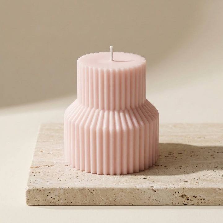 A two-tiered pink ribbed candle with a single wick, displayed on a light beige stone slab against a warm beige background.