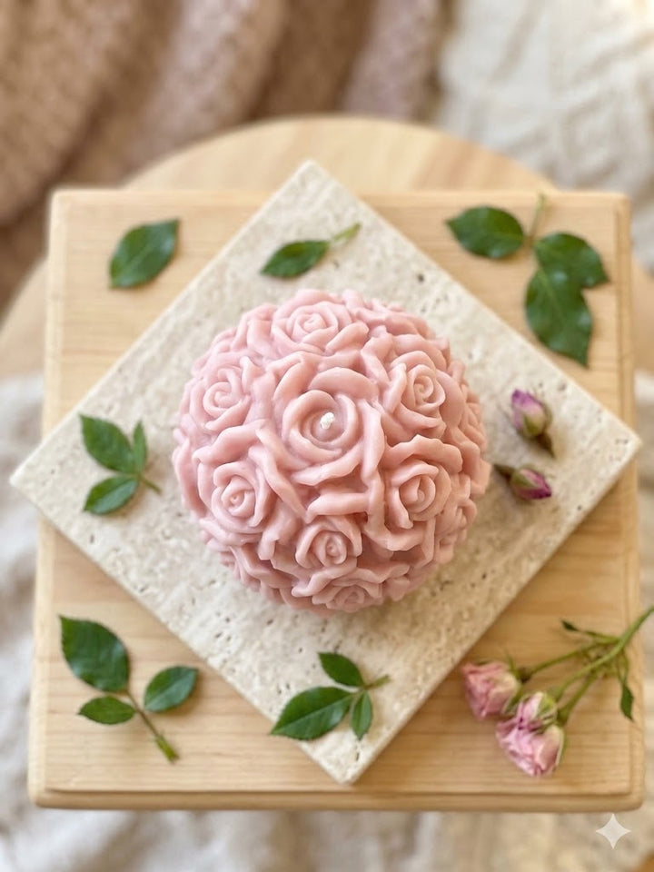 Pink rose-shaped soy wax candle on wooden block with green leaves — handmade in USA