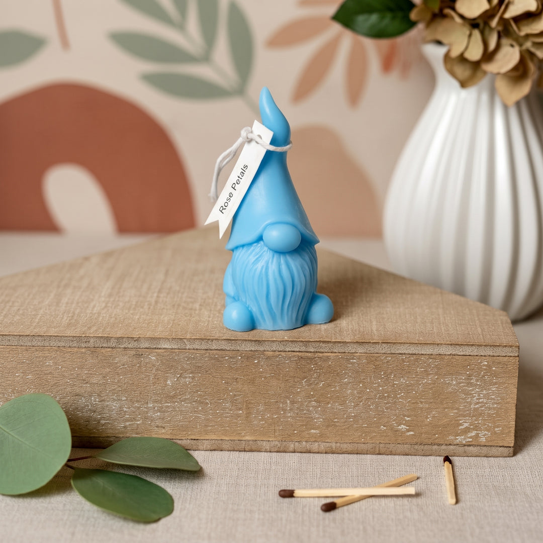 A small blue gnome figurine with a pointed hat and long beard sits on a wooden box. A white tag tied to the hat reads &
