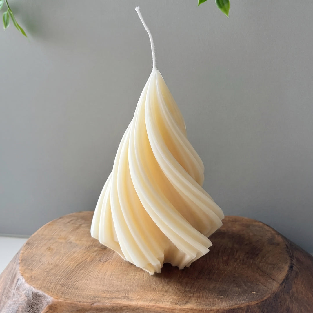 A spiral-shaped candle made from natural beeswax, standing upright on a rustic wooden block against a neutral gray background.