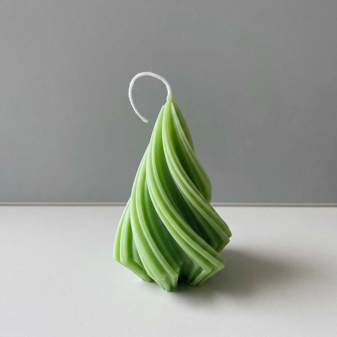 A green spiral-shaped candle with a white wick, standing upright on a white surface against a gray background.