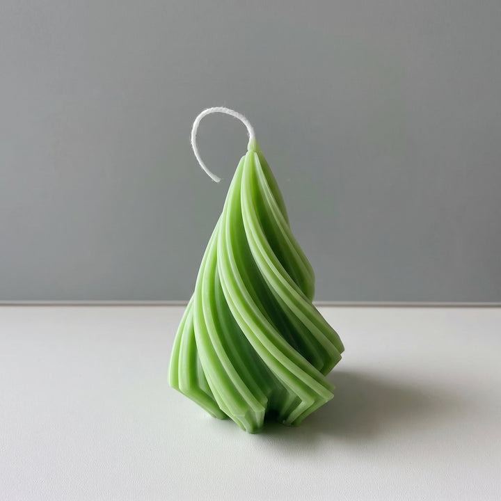 A green spiral-shaped candle with a white wick, standing upright on a white surface against a gray background.