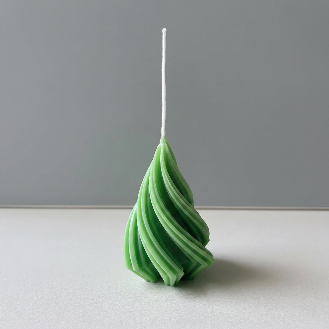 A spiral-shaped green candle with a white wick, standing upright on a white surface against a gray background.