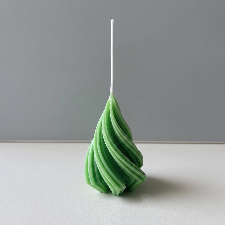 A spiral-shaped green candle with a white wick, standing upright on a white surface against a gray background.