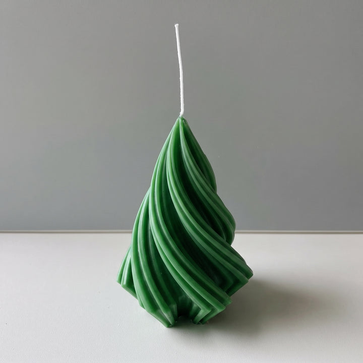 A green spiral tree-shaped candle with a white wick, standing upright on a white surface against a gray background.