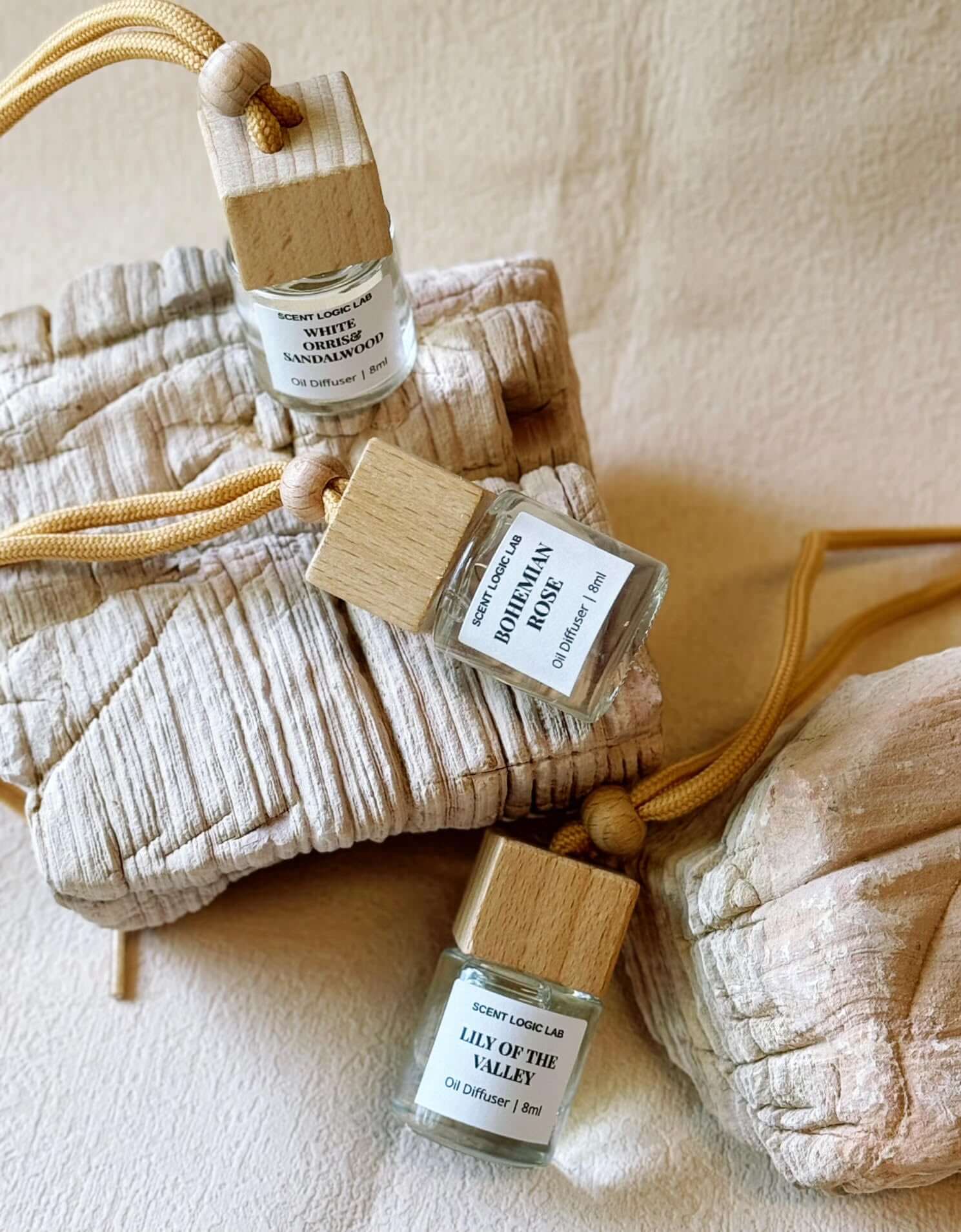 Three artisan car diffusers with wooden caps on a textured fabric background, showcasing unique fragrances.