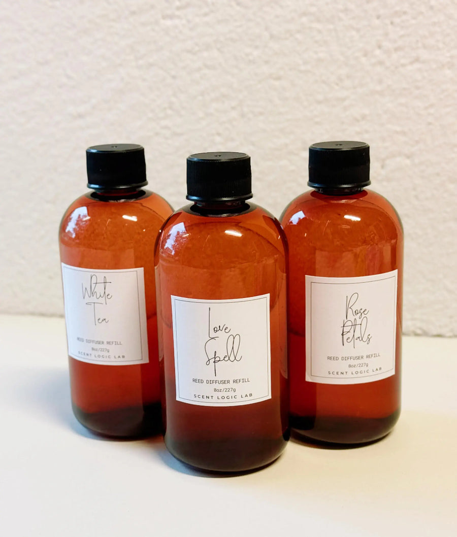 Three amber bottles of reed diffuser refills labeled White Tea, Fall Spell, and Rose Petal.